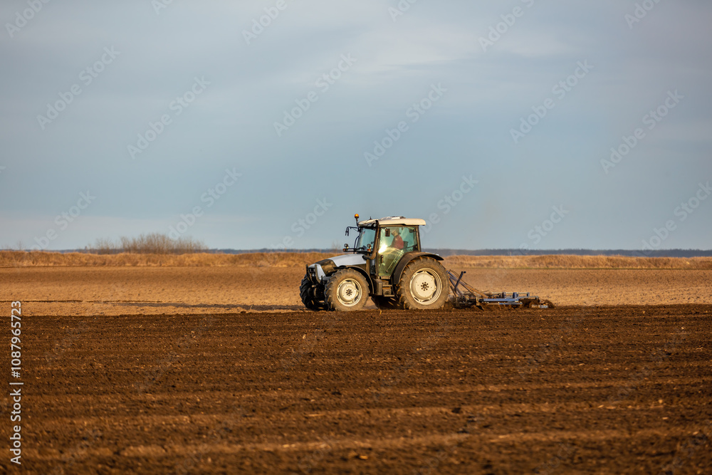 Tractor with a plow attachment tilling the soil in a vast farmland setting Tractor with a plow attachment tilling the soil in a vast farmland setting