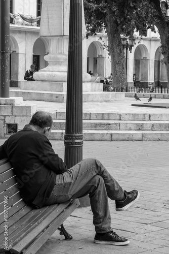 Hombre sentado en un banco de plaza blanco y negro