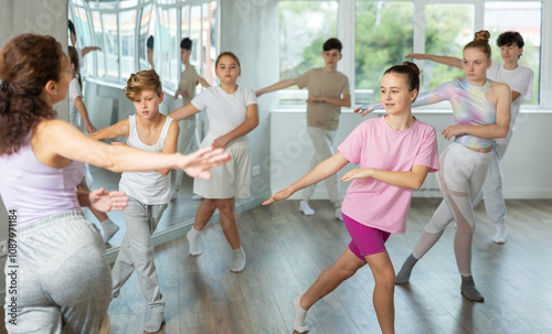 Female girl student repeats movements of unrecognizable teacher during group modern dance class. Hobbies, active pastime, additional extracurricular activities for children and teenagers photo