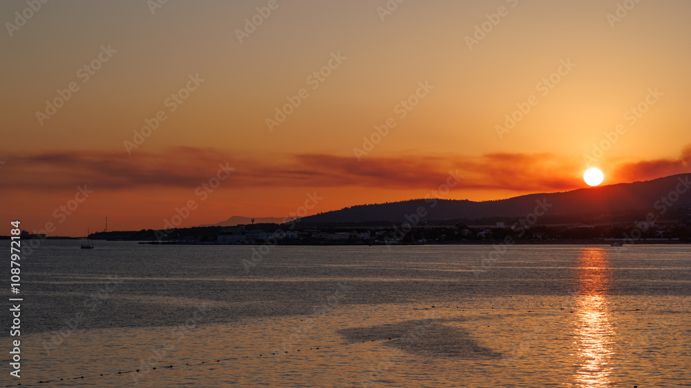 Sunset over the Coastal City. Dramatic sunset over the sea, fiery sky, silhouette of a city. Golden hour, coastal landscape, evening scene, vacation vibes. Sunset over the Coastal City. Dramatic sunset over the sea, fiery sky, silhouette of a city. Golden hour, coastal landscape, evening scene, vacation vibes.