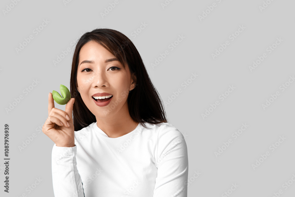 Young Asian woman with fortune cookie on grey background Young Asian woman with fortune cookie on grey background
