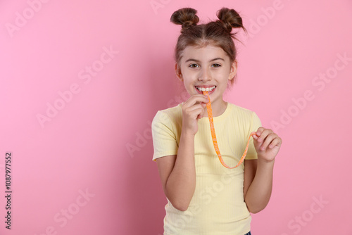 Happy girl eating tasty gummy candy on pink background. Space for text