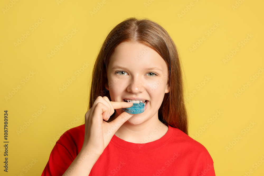 Teenage girl eating tasty gummy candy on yellow background Teenage girl eating tasty gummy candy on yellow background