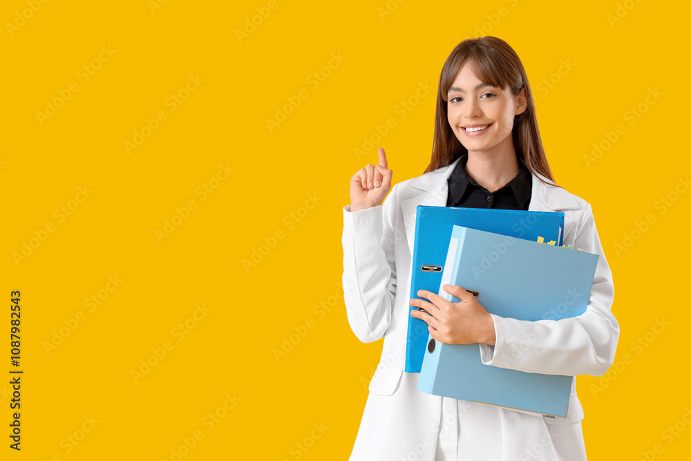 Beautiful businesswoman with folders pointing at something on yellow background Beautiful businesswoman with folders pointing at something on yellow background