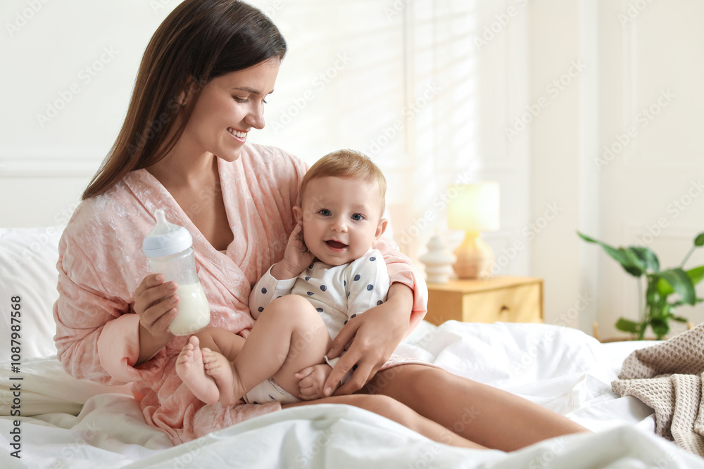 Mother holding cute little baby and bottle of milk on bed at home. Space for text Mother holding cute little baby and bottle of milk on bed at home. Space for text