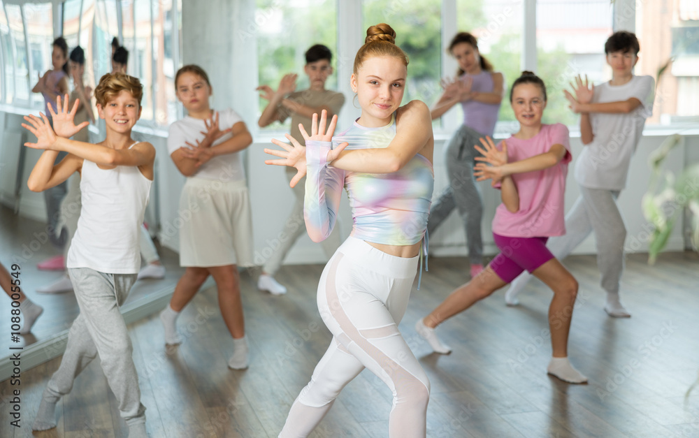 Naklejka premium Teenagers in classroom dance and learn modern dances, participants of lesson move in staggered manner to beat of energetic music. Female teacher in background dances with students