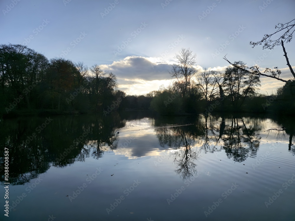 Obraz premium A body of water surrounded by trees and clouds