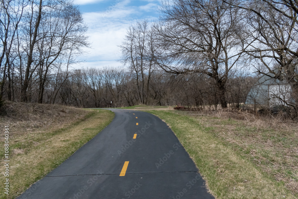 Fototapeta premium A paved walking path at a local Minnesota park surrounded by grass and trees.