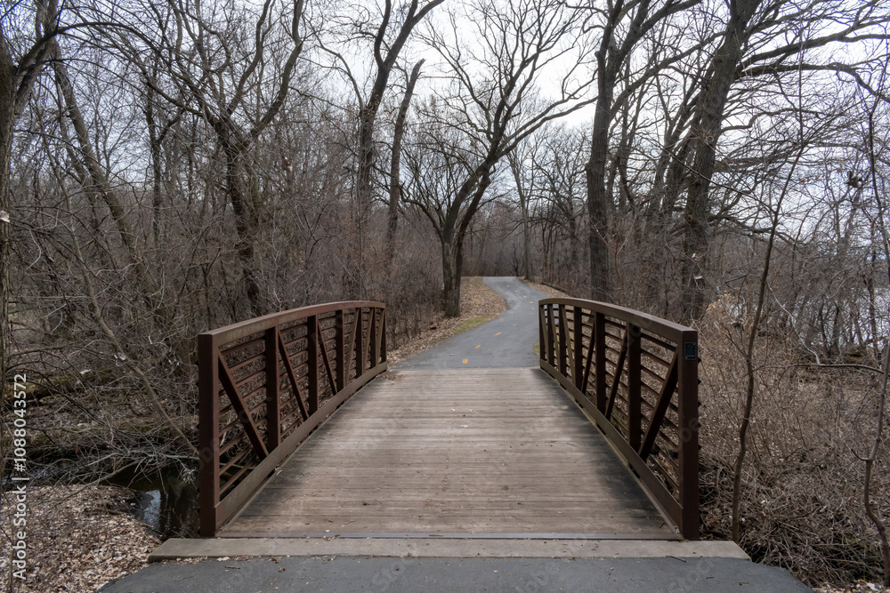 A paved path at a local Minnesota park leads to a walking bride during Autumn. A paved path at a local Minnesota park leads to a walking bride during Autumn.