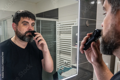 Man shaving his beard in the bathroom. Beard care, electric razor. photo