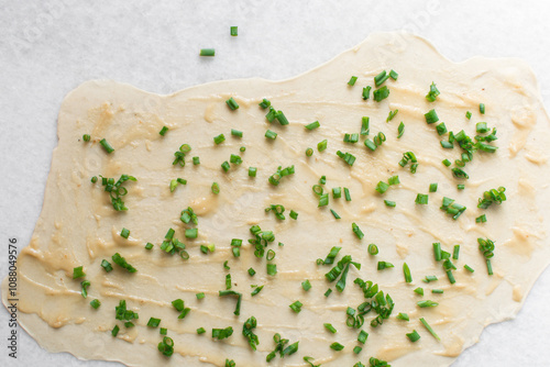 Overhead view of green scallions on oiled pancake dough, top view of sliced green onion on rolled out scallion pancake dough, process of making flaky scallion pancake