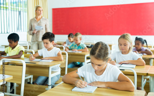 Multiracial group of kids working at class, writing and listening explanations of teacher in classroom