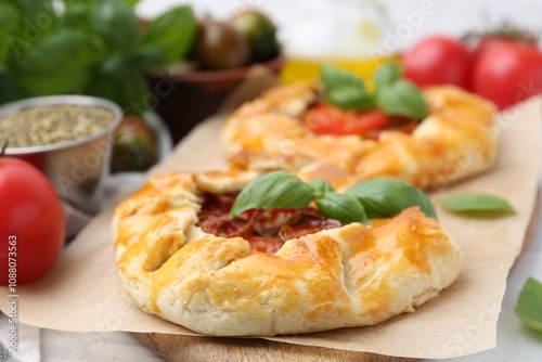 Tasty galettes with tomato and basil on white tiled table, closeup