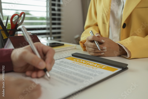 A man signs a contract after agreeing to buy a house with an agent. The agent explains the details of the contract to the buyer before signing it. Home purchase contract photo