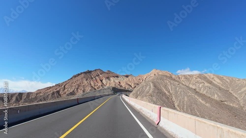 Driving on asphalt road passing through Gobi desert with colorful mountains on sunny autumn day in southern Xinjiang, China, POV from the car, 4k real time footage, travel concept. photo