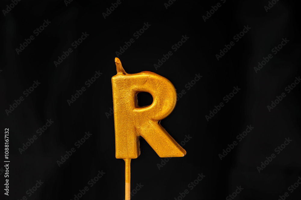 close up on gold Letter R birthday candle on a dark background.
close up on gold Letter R birthday candle on a dark background.