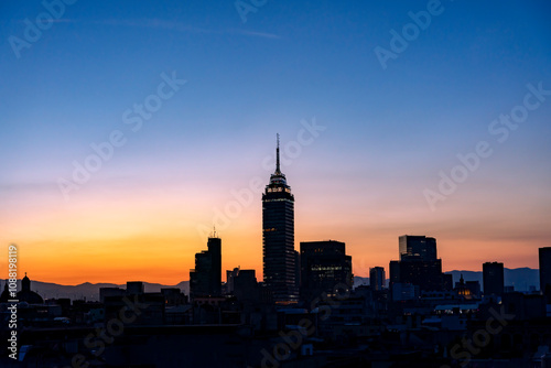 The Mexico City skyline at sunset, featuring Torre Latinoamericana and other buildings silhouetted against a colorful orange and blue sky. photo