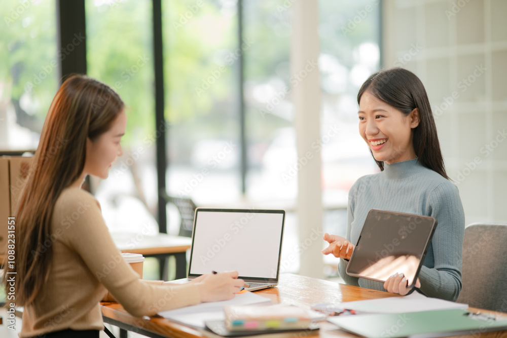 Two Asian businesswomen working with documents in an office.