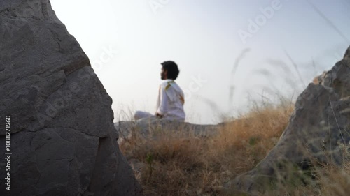 young Indian yogi doing his yoga mediation practices on hills rocks in forest