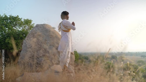 young Indian yogi doing his yoga mediation practices on hills rocks in forest