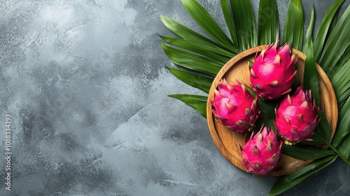 Vibrant dragon fruit arranged on a palm leaf inside a wooden plate, set against a textured gray stone background with ample copy space for text. photo