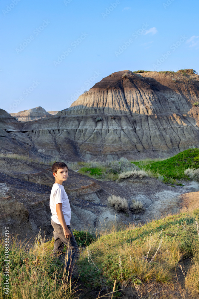 Naklejka premium Teenage hiker boy is standing among eroded formations in canyon.