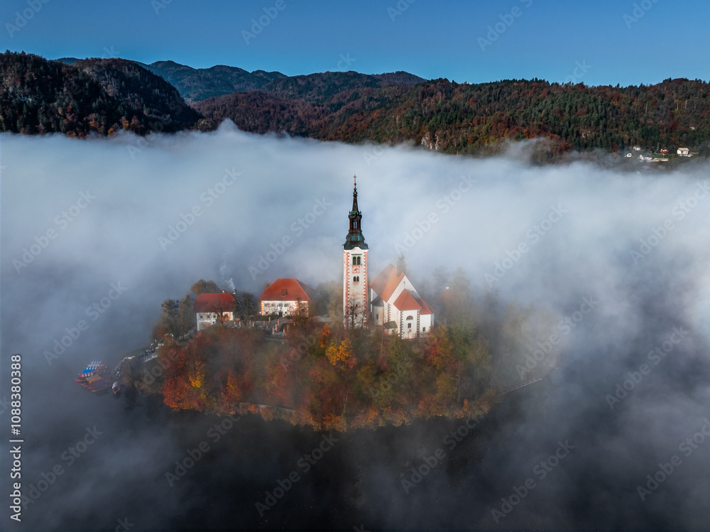 Bled, Slovenia - Beautiful foggy autumn sunrise at Lake Bled with the famous Pilgrimage Church of the Assumption of Maria (Bled Island) covered in fog on an October morning. Clear blue sky