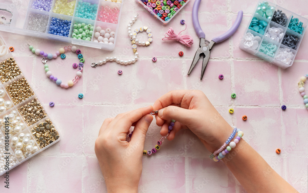 Child making beaded bracelets at home on pink tiled table