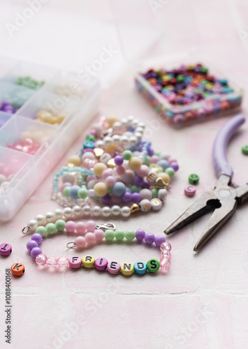Colorful beads and pliers arranged on pink tile for jewelry making