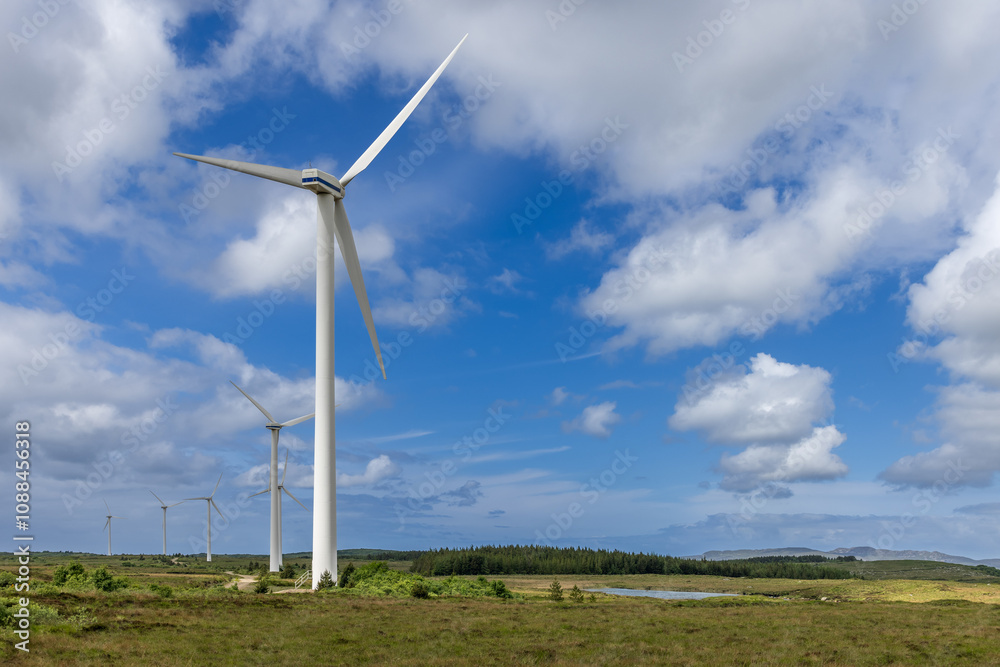 Fototapeta premium Wind turbines stretch into the distance against a vast sky and fields in Ireland, showcasing a blend of nature and renewable energy