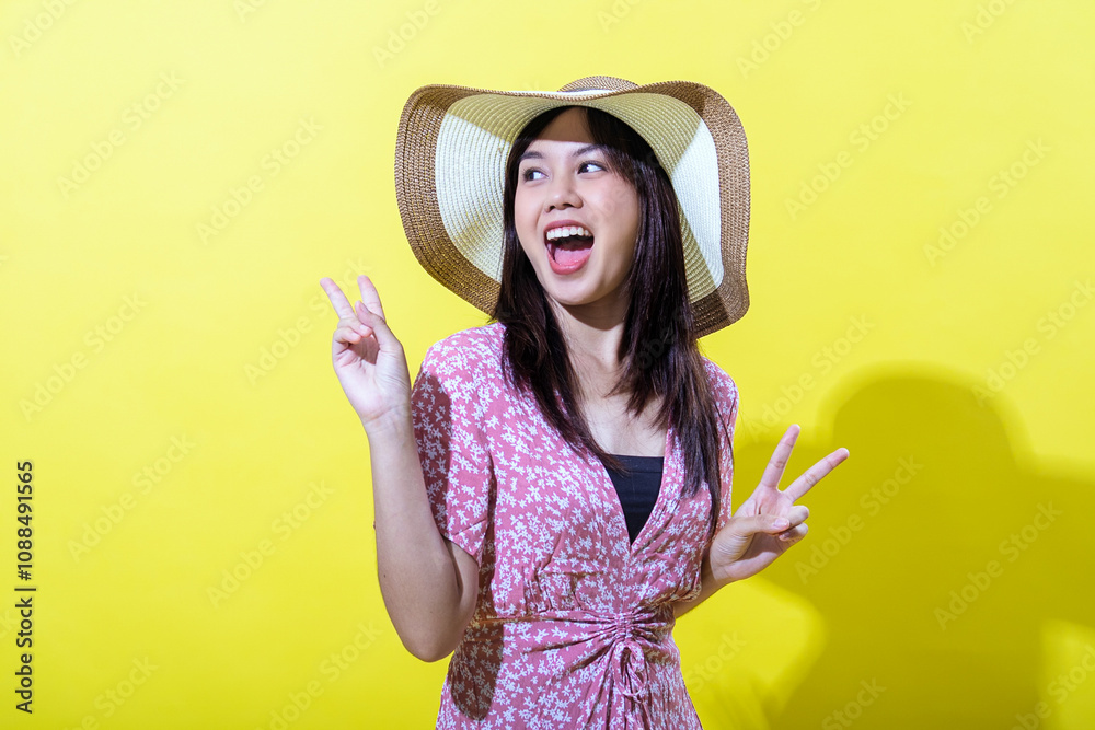 Asian woman in a pink floral dress, wearing a wide-brimmed straw hat, smiling brightly and making peace signs with both hands against a vibrant yellow background, radiating joy and positivity Asian woman in a pink floral dress, wearing a wide-brimmed straw hat, smiling brightly and making peace signs with both hands against a vibrant yellow background, radiating joy and positivity
