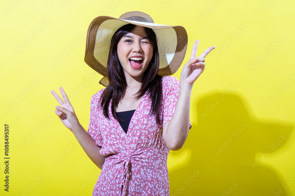 Asian woman in a pink floral dress, wearing a wide-brimmed straw hat, smiling brightly and making peace signs with both hands against a vibrant yellow background, radiating joy and positivity Asian woman in a pink floral dress, wearing a wide-brimmed straw hat, smiling brightly and making peace signs with both hands against a vibrant yellow background, radiating joy and positivity