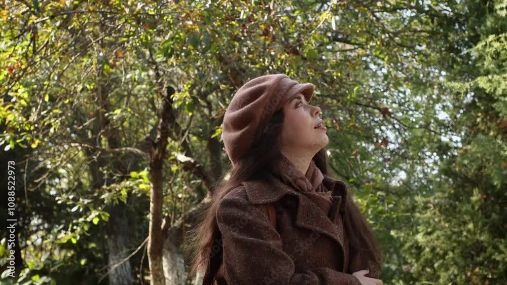 Side view of a young calm woman in a hat, buttoning her coat and admiring nature in an autumn park. The concept of psychology Side view of a young calm woman in a hat, buttoning her coat and admiring nature in an autumn park. The concept of psychology