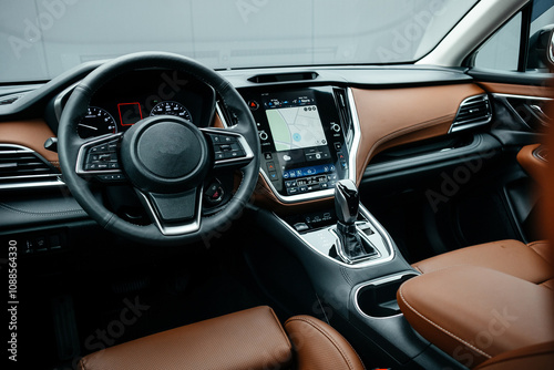 Modern brown car interior, leather steering wheel, climate control, large navigation screen, air ducts, deflectors on the car panel. Interior details.