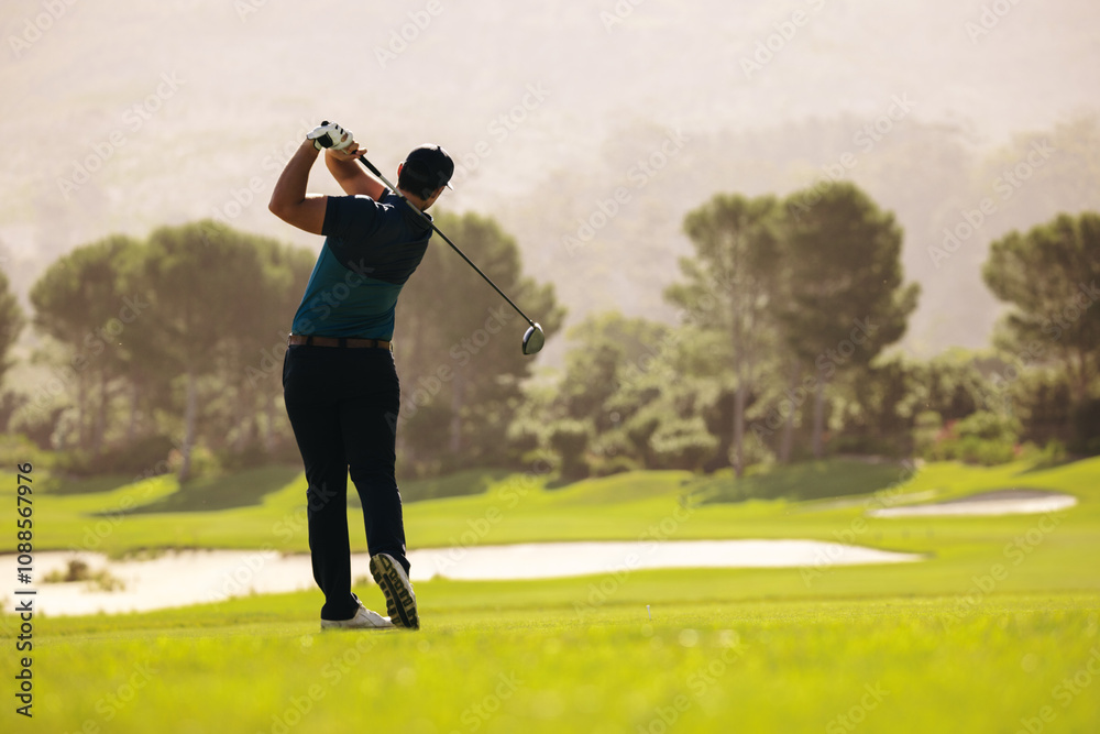 Male golfer swinging golf club with a powerful follow through on a sunny fairway Male golfer swinging golf club with a powerful follow through on a sunny fairway