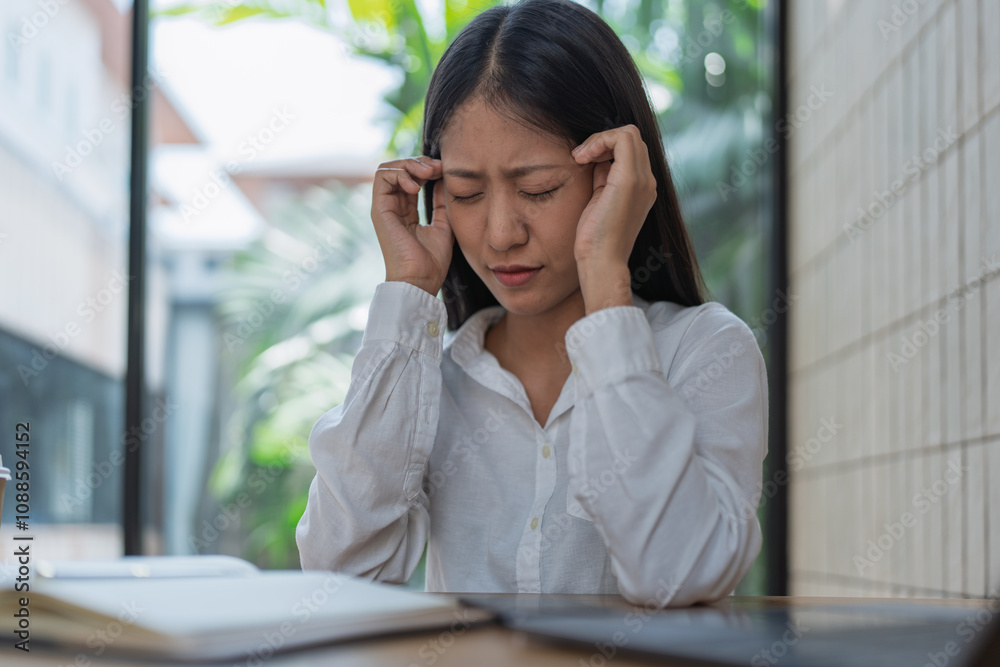 Young Woman in White Shirt Struggling with Stress and Headache While Sitting at a Modern Workspace Surrounded by Greenery and Natural Light Young Woman in White Shirt Struggling with Stress and Headache While Sitting at a Modern Workspace Surrounded by Greenery and Natural Light