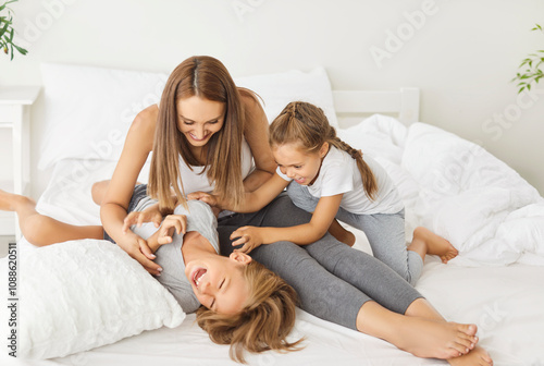 Obraz na plátne Family with kids playing and tickling each other on the bed at home