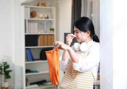 A young woman wearing orange rubber gloves covers her nose, which has an unpleasant odor clinging to the gloves, after finishing housework.