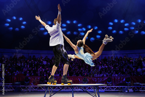 Young pair of acrobats, man and woman, on roller skates perform in a circus on a small round stage. photo