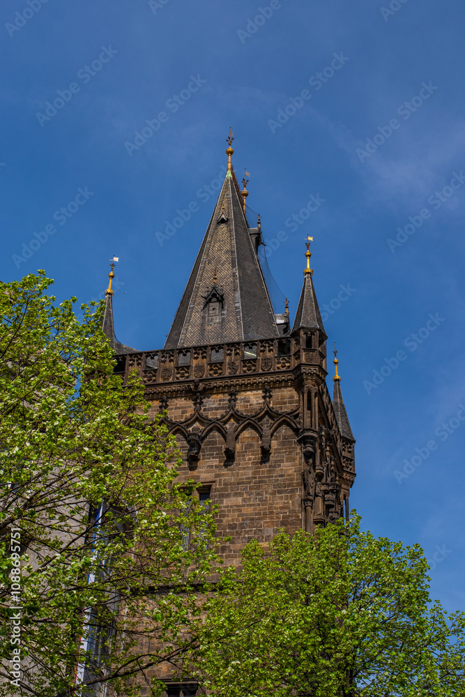 The upper section of the Powder Tower (Prašná brána), a famous Gothic structure in Prague, Czech Republic. The tower’s intricate stonework and dark facade are visible, with pointed arches. The upper section of the Powder Tower (Prašná brána), a famous Gothic structure in Prague, Czech Republic. The tower’s intricate stonework and dark facade are visible, with pointed arches.