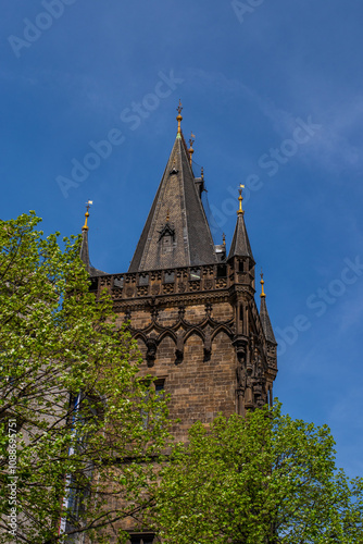 The upper section of the Powder Tower (Prašná brána), a famous Gothic structure in Prague, Czech Republic. The tower’s intricate stonework and dark facade are visible, with pointed arches.