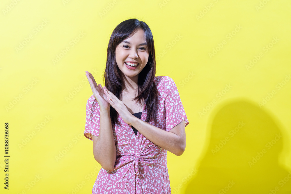 Indonesian Asian woman in a pink floral dress, smiling brightly against a yellow background. Bright, even lighting. Indonesian Asian woman in a pink floral dress, smiling brightly against a yellow background. Bright, even lighting.