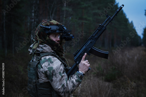 Special forces soldier with an assault rifle in camouflage and with a night vision device in a dark forest. photo