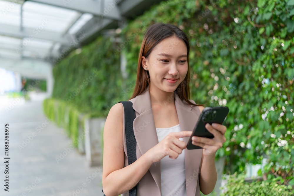 Asian Woman Using Phone While Walking Across a Greenery Background Asian Woman Using Phone While Walking Across a Greenery Background