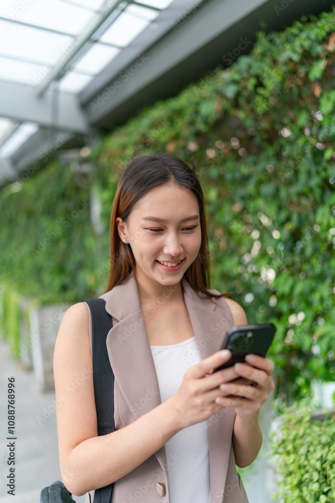 Asian Woman Using Phone While Walking Across a Greenery Background Asian Woman Using Phone While Walking Across a Greenery Background