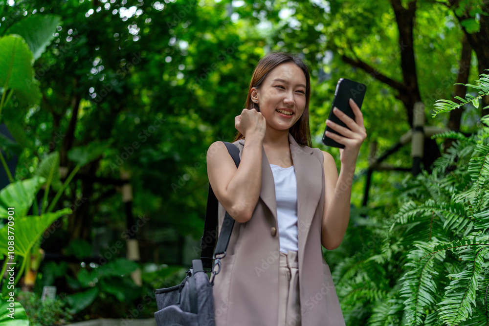 Asian Woman With Laptop Bag Using Phone Amid Greenery in A Park In the City Asian Woman With Laptop Bag Using Phone Amid Greenery in A Park In the City