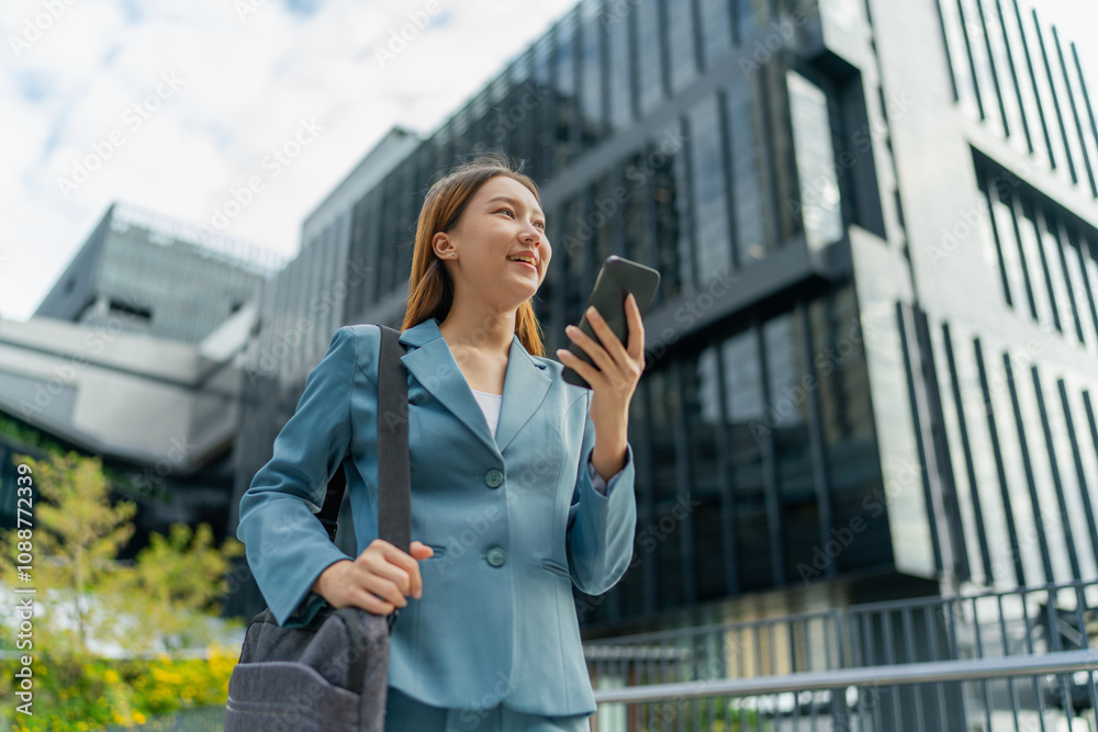 Asian Businesswoman Carrying Laptop Bag Using Phone In Front Of A Modern Office Building Asian Businesswoman Carrying Laptop Bag Using Phone In Front Of A Modern Office Building