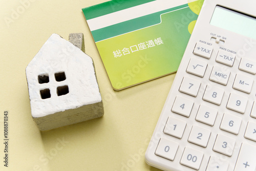 電卓と預金通帳とミニチュアの家