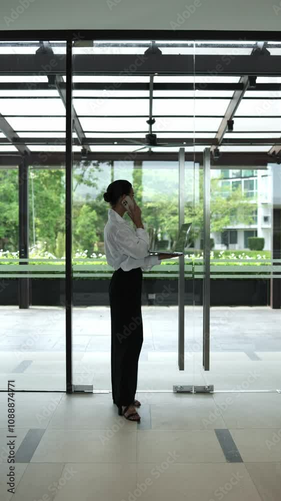 Panoramic view from skyscraper building. Businesswoman standing near window in new modern office and talking by smartphone. Communication, management and productive work concept. Vertical shot Panoramic view from skyscraper building. Businesswoman standing near window in new modern office and talking by smartphone. Communication, management and productive work concept. Vertical shot