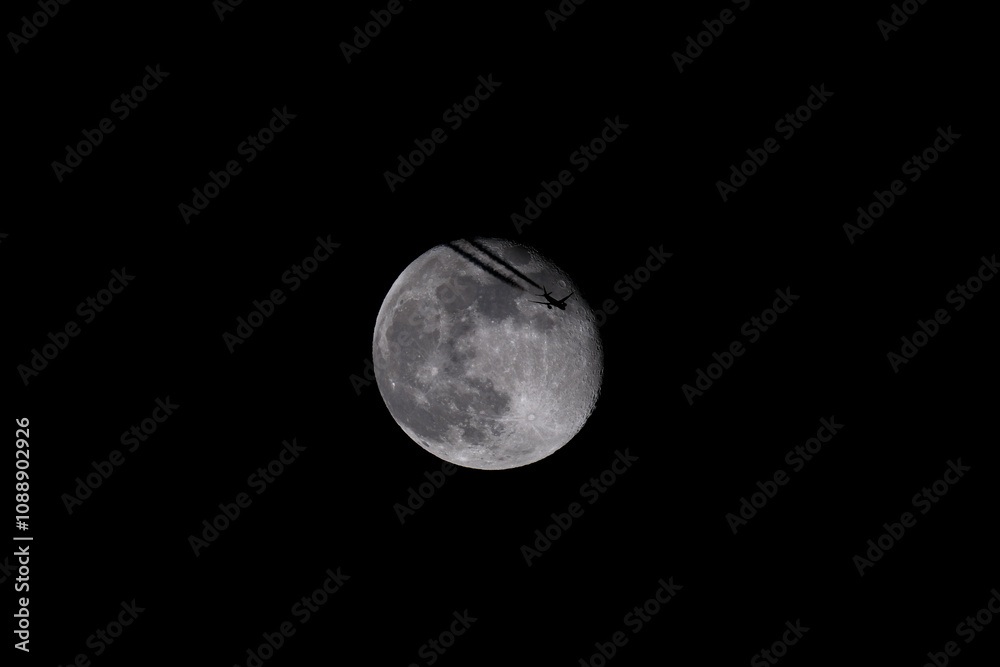 Obraz premium The moon in the night sky with a silhouette of an airplane. The moon in the dark sky with a plane flying over it.